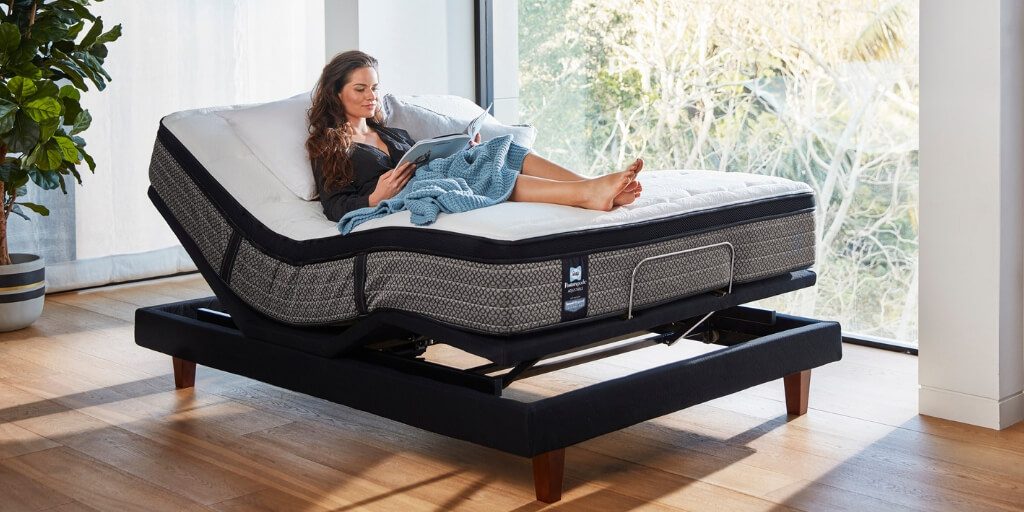 Young woman lies on a Sealy adjustable bed reading a book